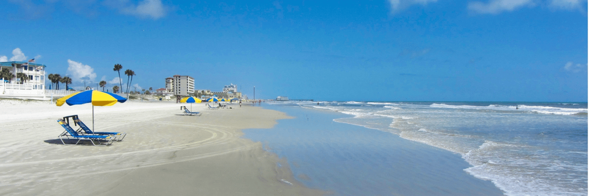 Daytona Beach with the surf washing up on the sand and beach chairs with umbrellas lining the coast