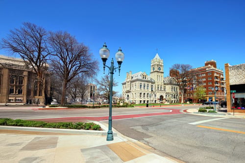 Sunny day in Downtown Manhattan, Kansas, with historic buildings, a clock tower, and a quiet street scene framed by bare trees