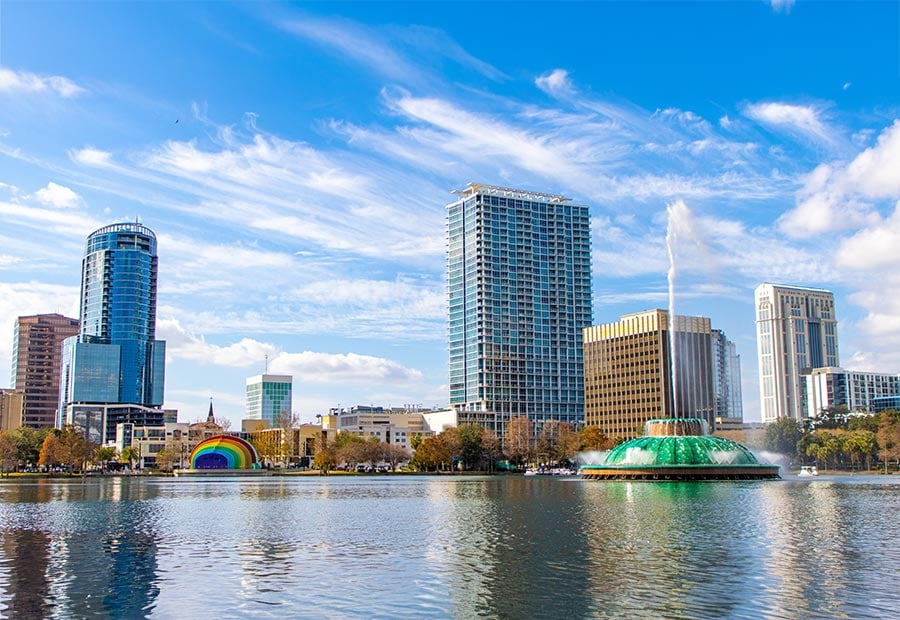 Lake Eola fountain and downtown Orlando skyline under a bright blue sky.