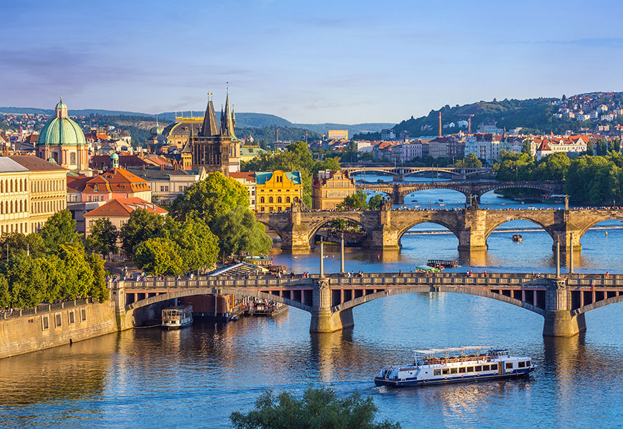 Historic bridges spanning the Vltava River with Prague's skyline and church spires in the background.