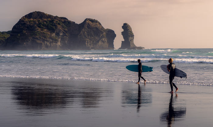 Surfers in Piha, Auckland, New Zealand, with Lion Rock in the background.