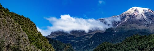 Vista panorámica del Nevado del Tolima con su cima nevada y rodeado de exuberante vegetación bajo un cielo azul. Descubre la belleza natural de Ibagué y sus alrededores, y encuentra vuelos para explorar la 'Capital Musical de Colombia'