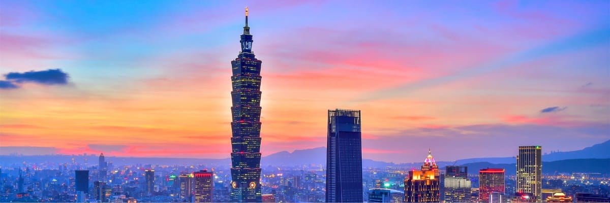 Colorful sunset over Taipei featuring Taipei 101 rising above modern city buildings and mountain silhouette.