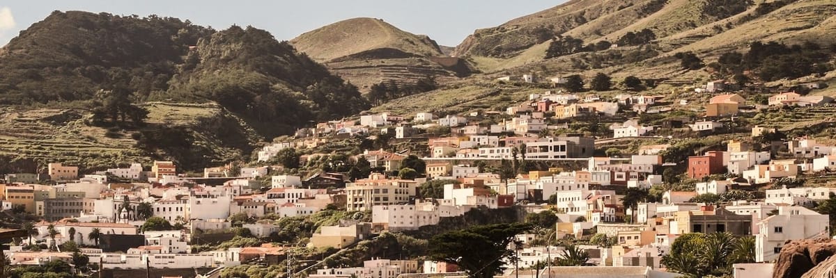 Clustered hillside village with white and pastel homes nestled among green terraces and rugged mountains.