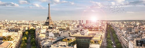 Panoramic view of Paris, France, featuring the iconic Eiffel Tower prominently on the left and a radiant sunset on the right.