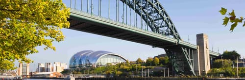 Tyne Bridge in Newcastle upon Tyne, England, with music venue visible in the background on a sunny day