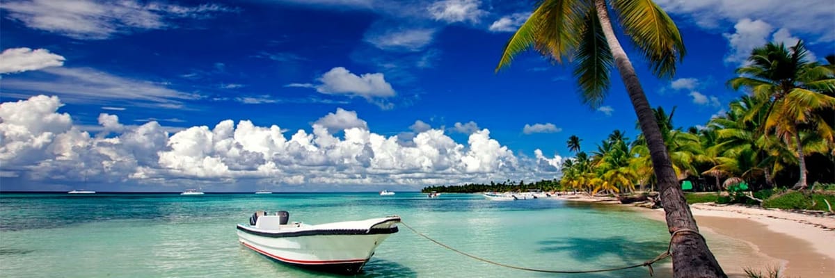 Beach in Punta Cana with boat floating in the water tied to a palm tree