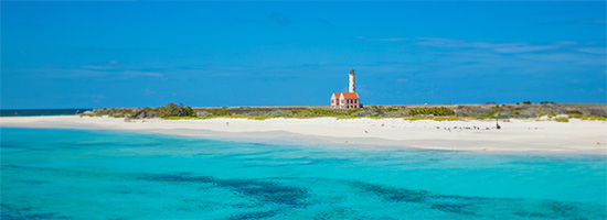 Faro de Klein Curazao en una isla de paisaje seco, arena clara y cielo despejado.
