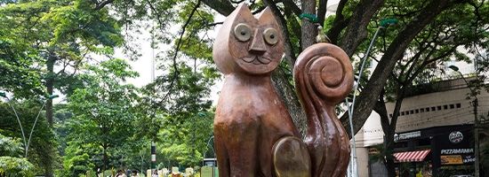 Escultura de bronce en el Parque del Gato del Río en Cali rodeada de vegetación.