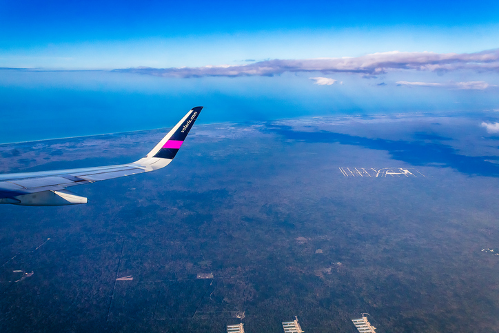 The wing of a Volaris airbus flying above the land and sea of Mexico.