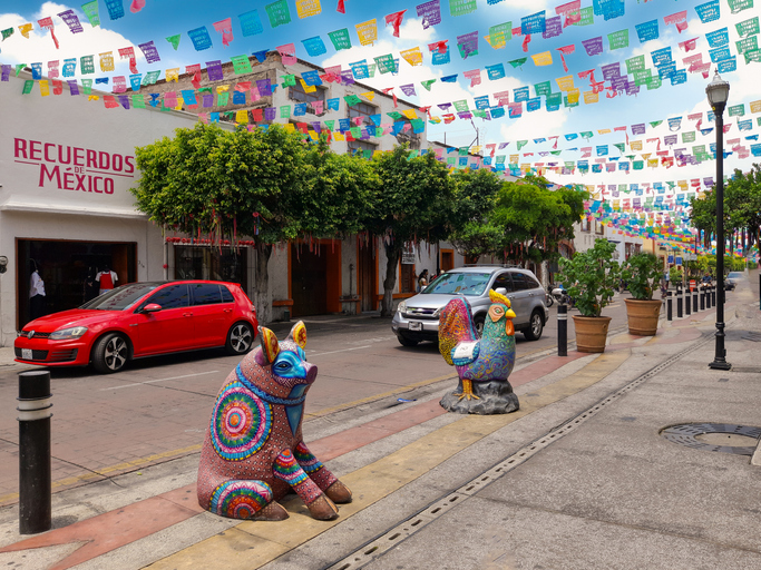 Colorful streets of Tlaquepaque, with Mexican flags hanging from the ceilings and status of spirit animals on the sidewalk.