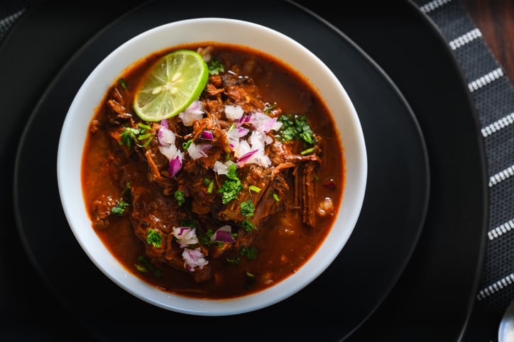 Served birria stew with mexican meat in a black plate.