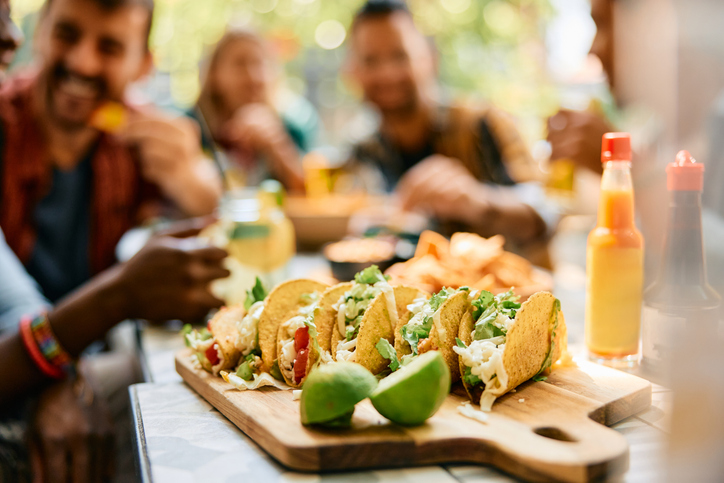 Served tacos on a wooden table, and a group of friends in the background. 