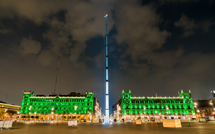 Flagpole and historic building of Plaza de la Constitución in Mexico City illuminated at night.