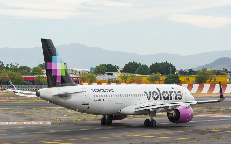 Avión de Volaris rodando en la pista del aeropuerto de Puebla, listo para el despegue bajo cielo nublado.