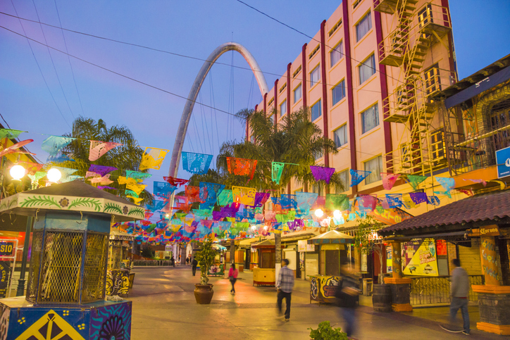Calle peatonal del centro de Tijuana decorada con papel picado multicolor, llena de vida y comercios típicos.