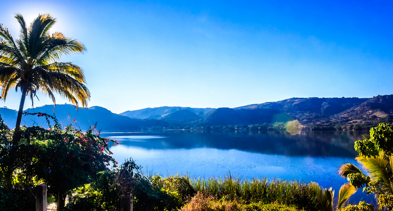 Vista panorámica de la laguna Santa María del Oro al amanecer, con montañas y palmera en primer plano.