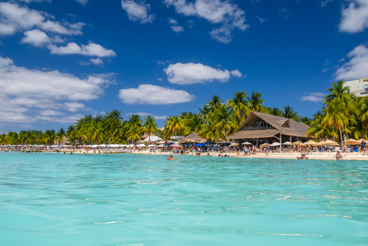 Playa Norte en Isla Mujeres, con turistas nadando y palapas rodeadas de palmeras.