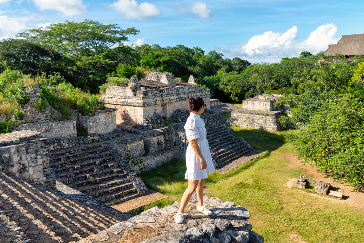 Turista sobre una pirámide en la zona arqueológica de Ek Balam, rodeada de vegetación tropical.