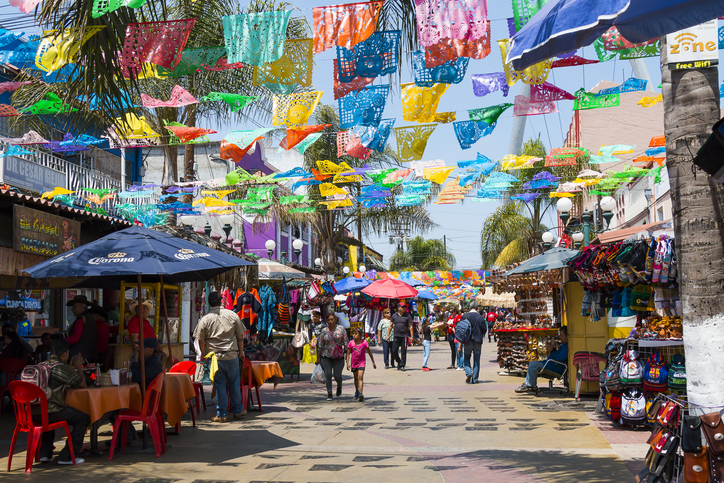 Calle peatonal decorada con papel picado y puestos de comida y artesanías en Tijuana.