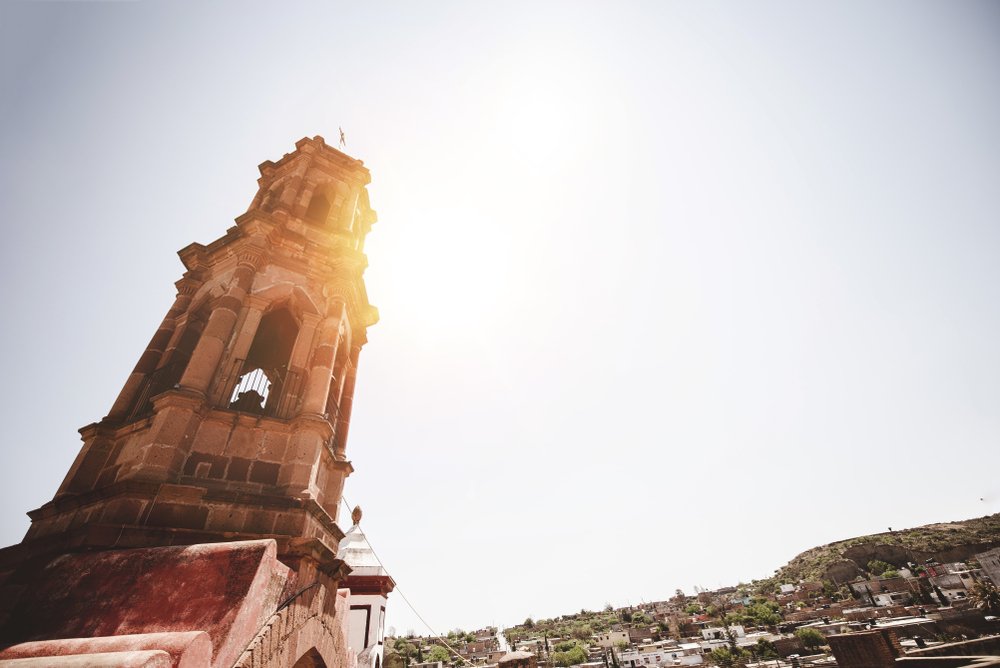 A low angle shot of a church bell tower with a bright sky in the background in Zacatecas.