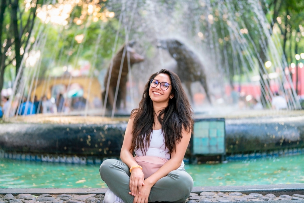 Joven sonriendo y sentada junto a la famosa Fuente del Coyote en Coyoacán, Ciudad de México, México.