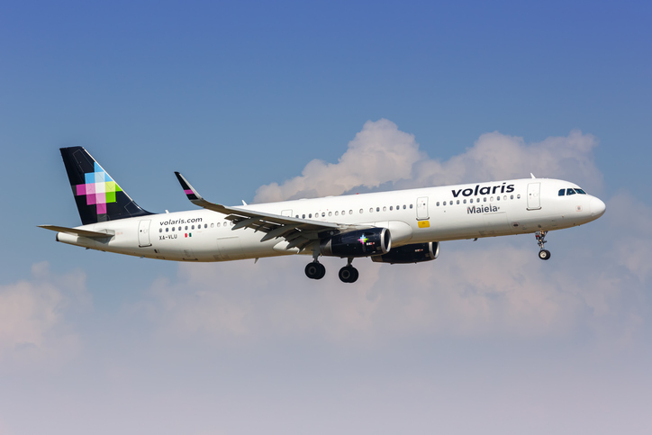 Volaris airbus flying across a slightly cloudy sky.