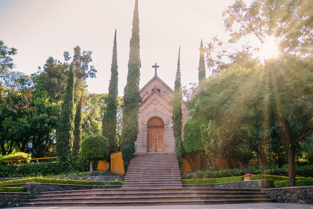 Beautiful church in Cerro de las Campanas, surrounded by trees and pines, and illuminated by sun rays.