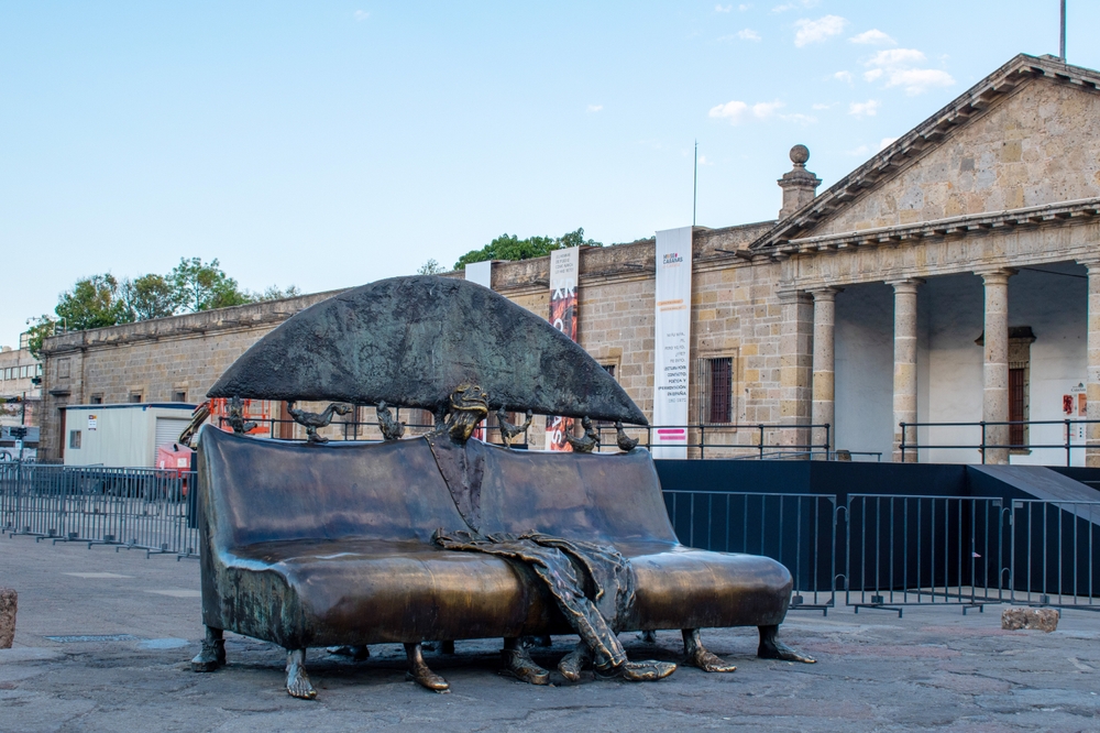 Escultura surrealista de bronce de un banco con una figura fundida frente al Instituto Cultural Cabanas en el centro de Guadalajara