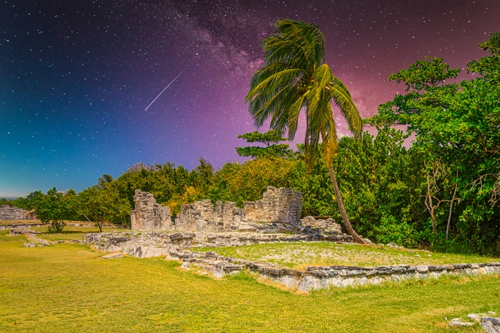 Imponentes ruinas de El Rey en Cancún al atardecer, con un cielo estrellado de fondo.