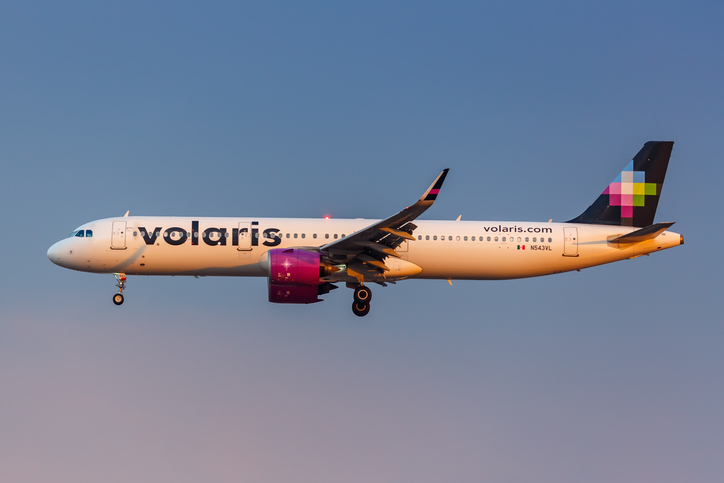 Volaris airbus flying across the sky at sunset.