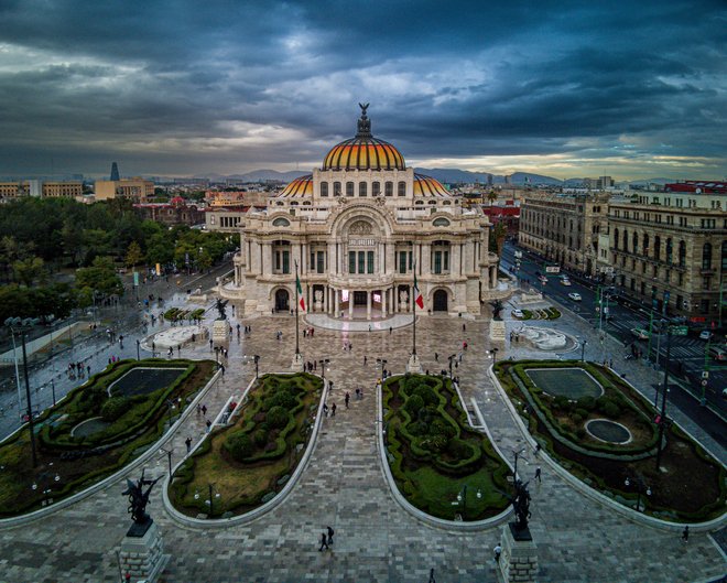 Vista aérea del Palacio de Bellas Artes en Ciudad de México con cielo nublado y jardines al frente.
