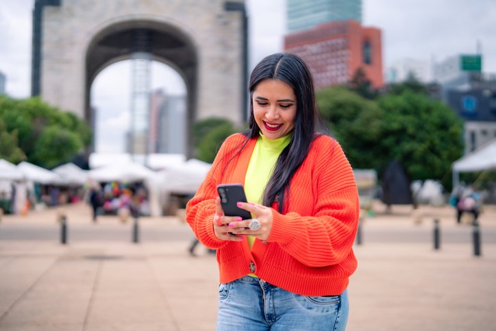 Turista en el Monumento a la Revolución de CDMX revisando su celular para organizar su itinerario.
