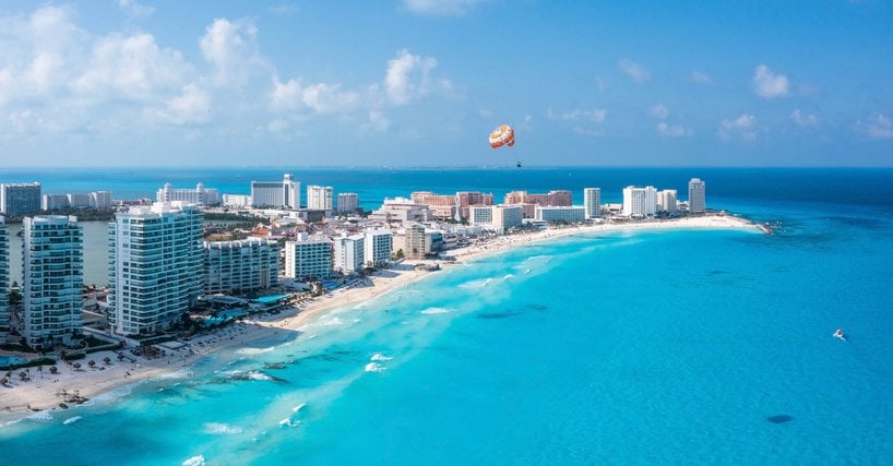 Vista aérea de la zona hotelera de Cancún con paracaídas sobrevolando el mar.