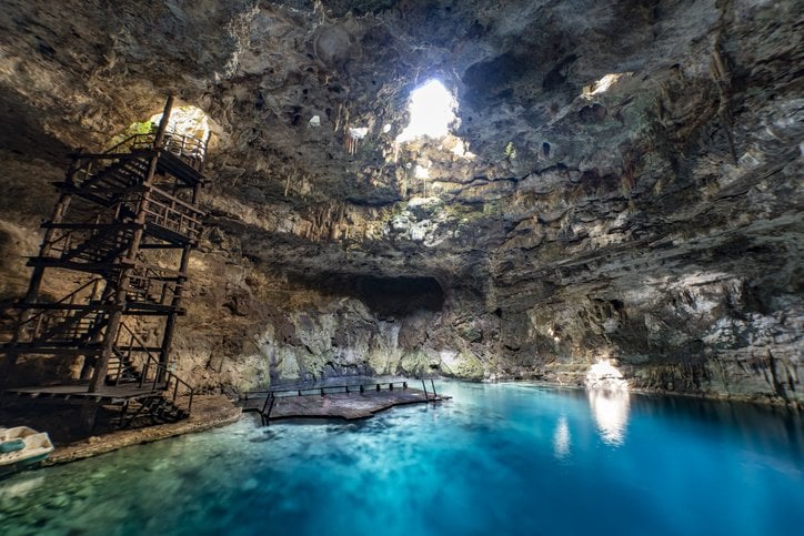 Interior de un cenote con agua azul y luz natural entrando desde arriba.