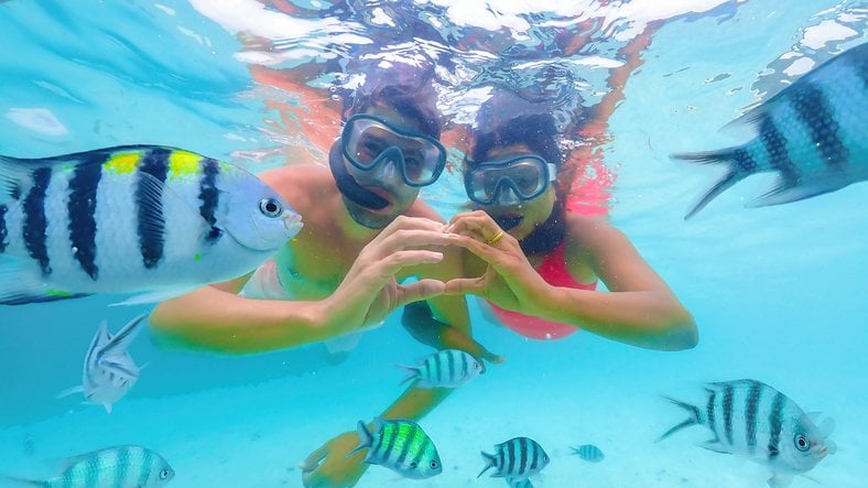 Pareja haciendo snorkel rodeada de peces en aguas cristalinas de Cancún.