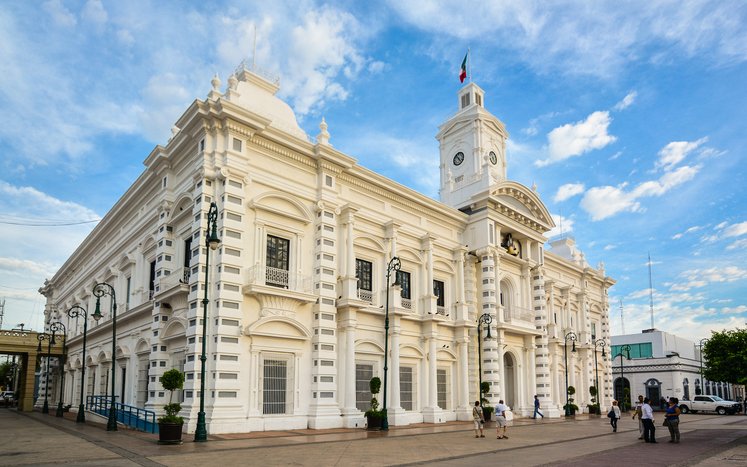 Palacio de Gobierno de Hermosillo con cielo azul y gente caminando frente al edificio.
