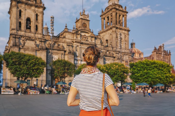 Mujer de espaldas observando la Catedral de la Ciudad de México en una mañana soleada.