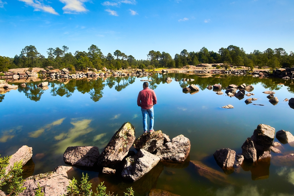 Joven frente a un lago con muchas rocas y bosques en el fondo de Mexiquillo, Durango.