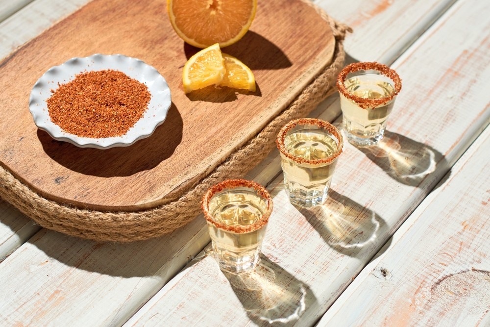 Shots de mezcal servidos con trozos de fruta naranja y ají