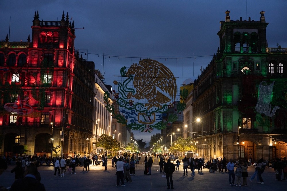 Emblema nacional de la bandera mexicana en el Zócalo de CDMX durante festividades patrióticas al anochecer.