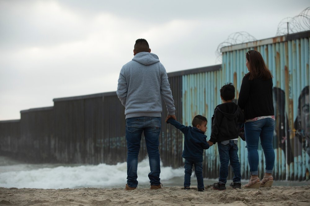 A family strolling through the shore of Playas de Tijuana, near the border wall.