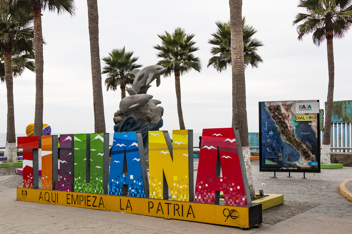 Colorido cartel de Tijuana con monumento y palmeras detrás.