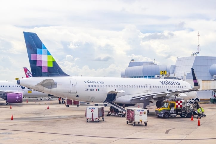 Avión de volaris rodeado de carros de carga de equipaje en el aeropuerto de Cancun