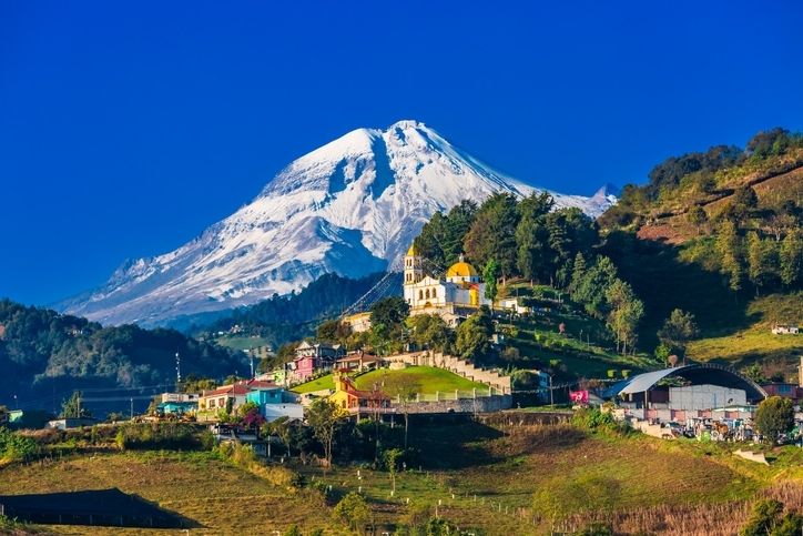 Volcán Pico de Orizaba y edificaciones cercanas sobre las colinas.