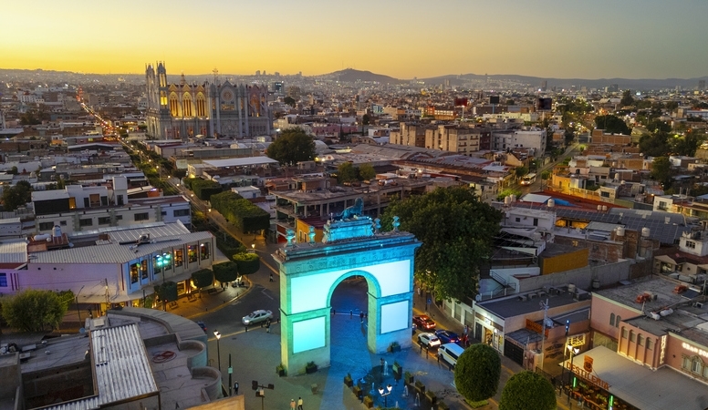 Vista aérea de la ciudad de León Guanajuato al atardecer, con el Arco de la Calzada iluminado en colores vivos..