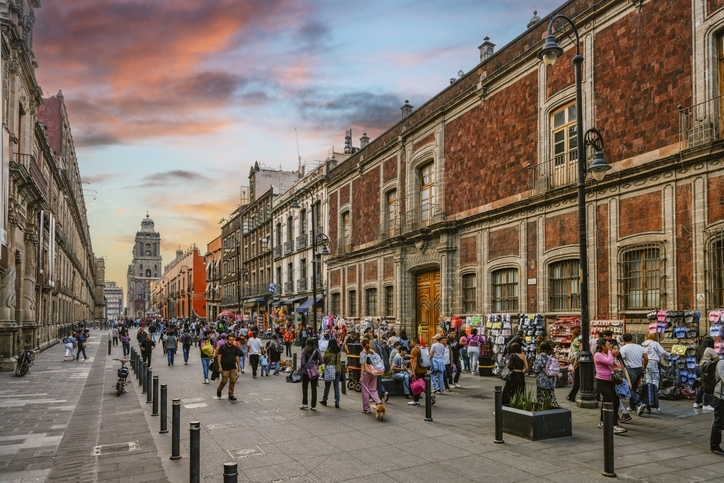 Gente caminando por la calle Moneda cerca del Zócalo, con la catedral de la Ciudad de México al fondo.