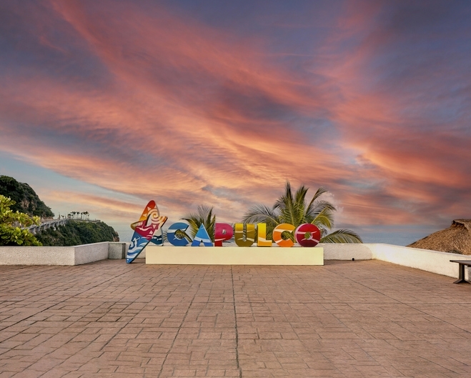 Cartel de Acapulco contra nubes rojizas al atardecer.