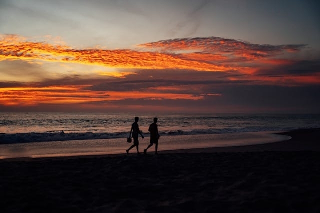 Dos personas caminando por la orilla del mar al atardecer.
