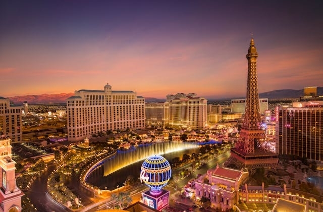Vista panorámica del Strip de Las Vegas al atardecer, con el hotel Bellagio, la Torre Eiffel del Paris Las Vegas y fuentes iluminadas.